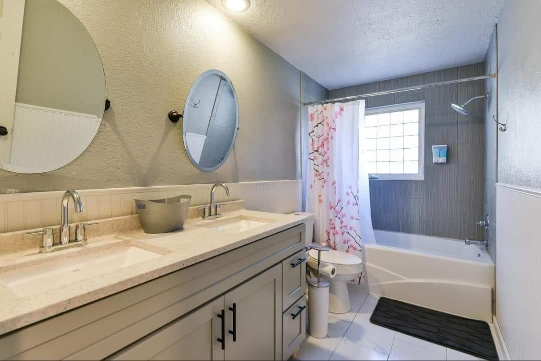 Bathroom with double sinks, tub, shower, and a floral shower curtain; gray and white color scheme.