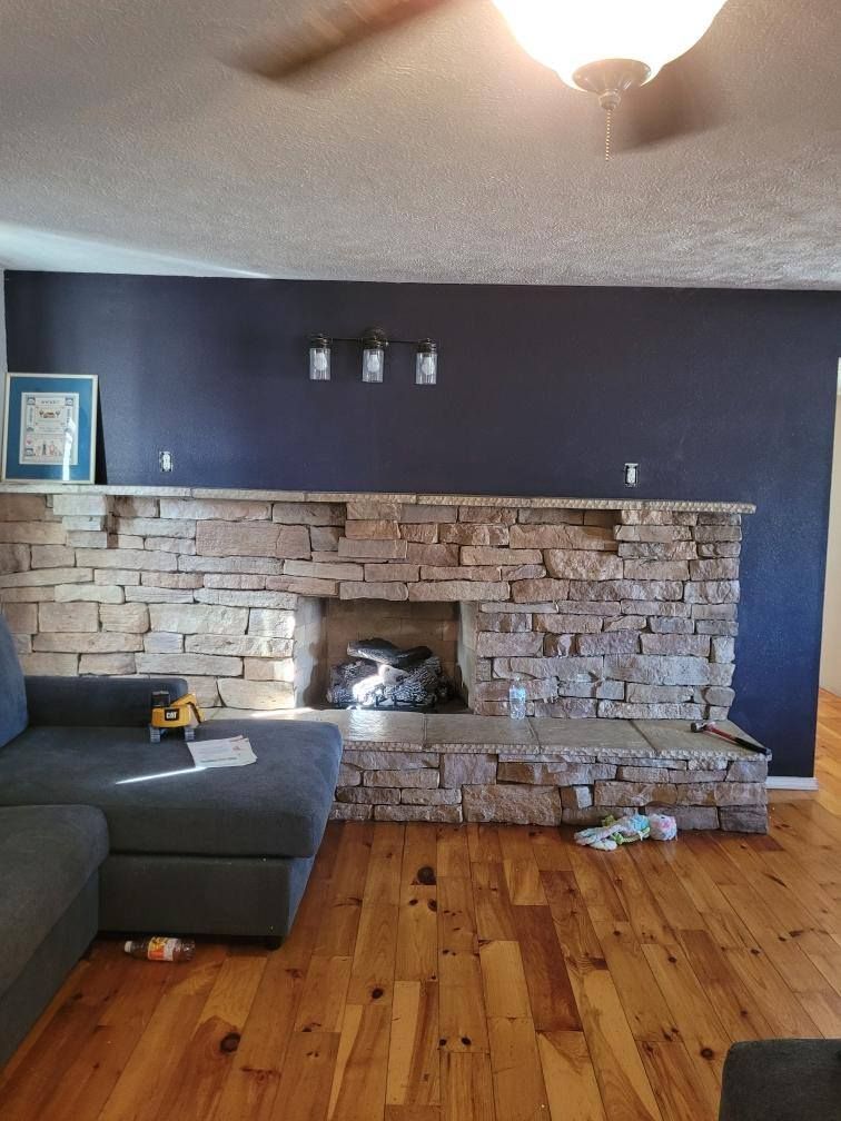 Stone fireplace with dark blue wall, wooden floors, and a grey sectional sofa.