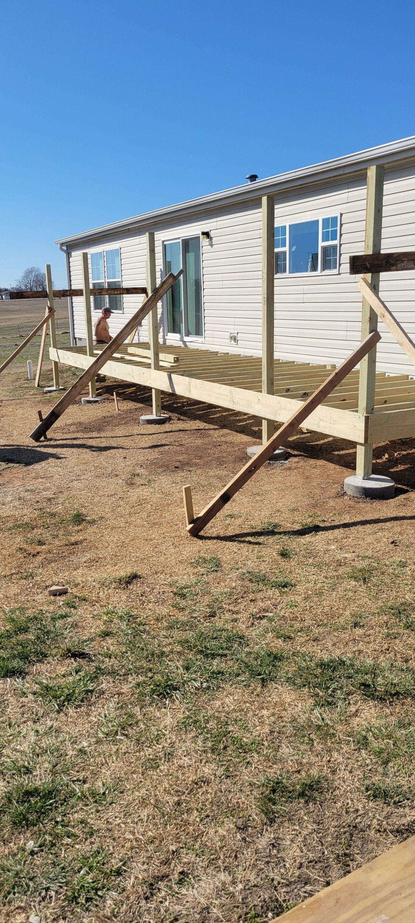 A deck under construction next to a mobile home, supported by angled wooden beams.