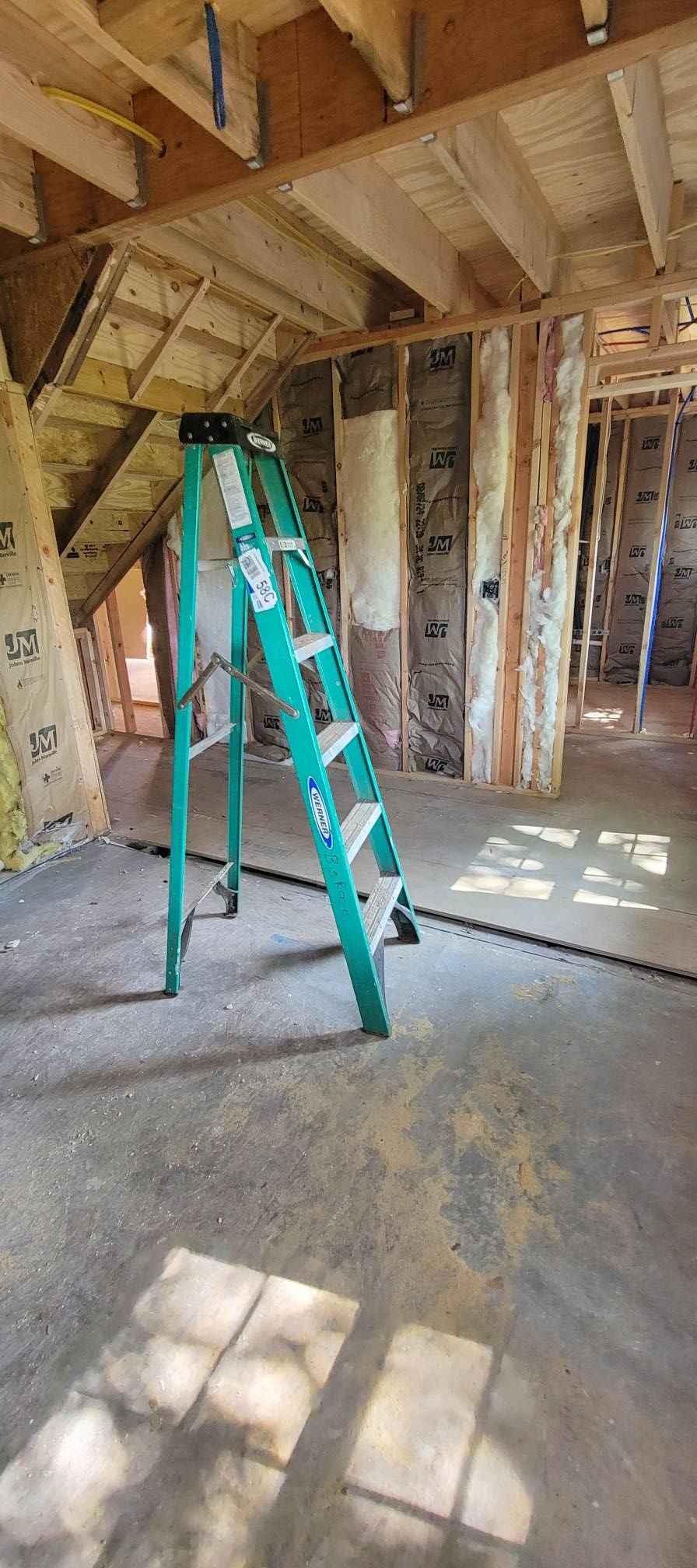 Interior of a room under construction with a green ladder. Wood beams and studs are visible.