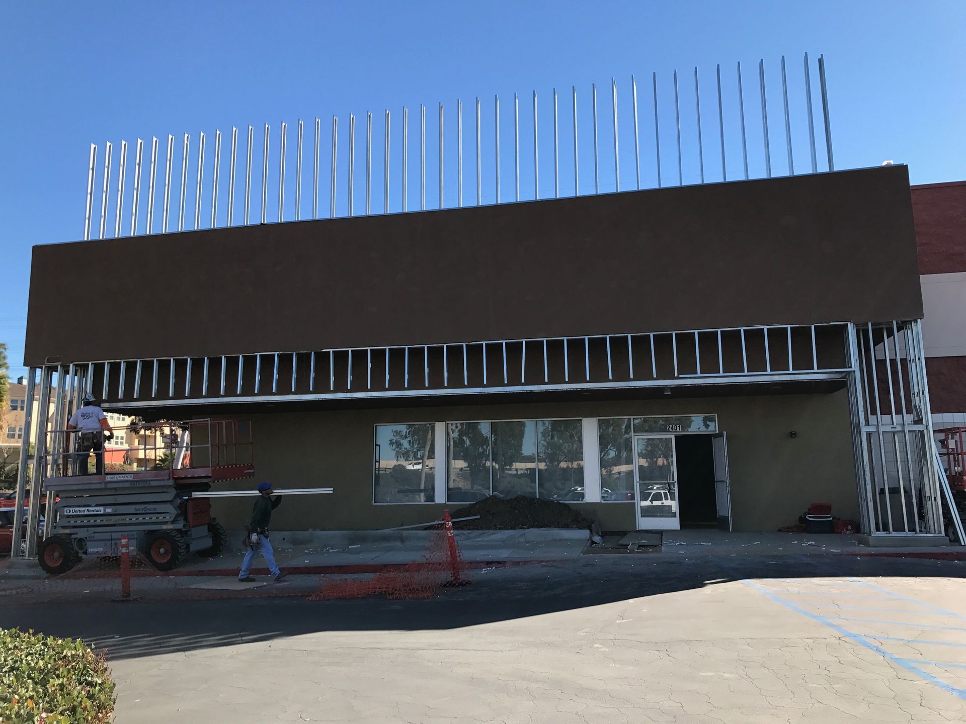 Building under construction; brown facade, exposed metal framing. People working; sky background.