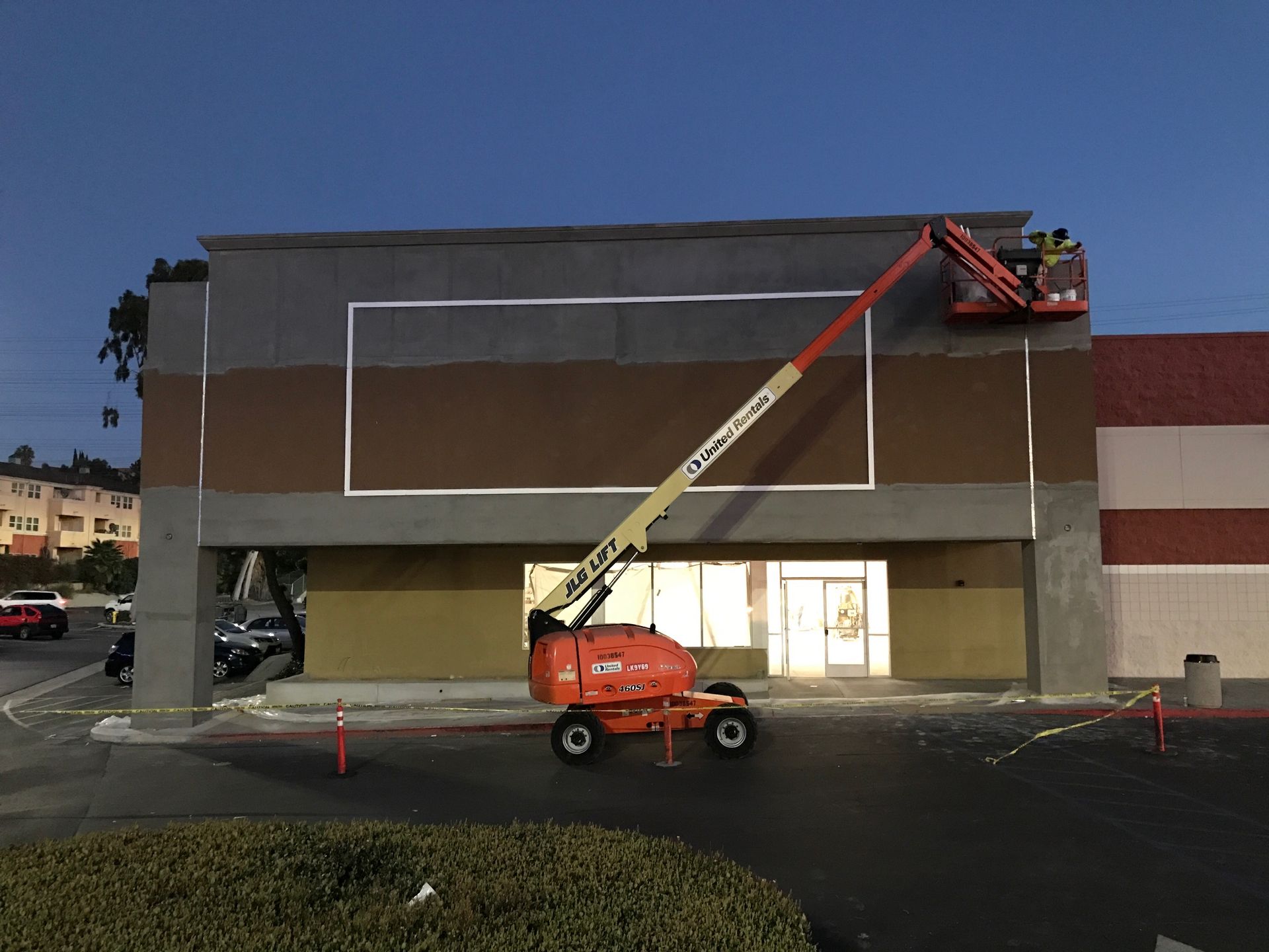Exterior of a building under renovation, workers on an aerial lift painting the facade.