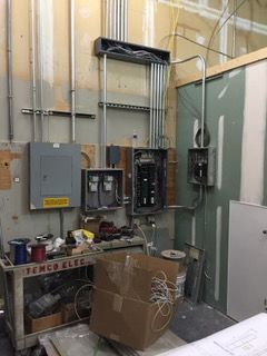 Electrical wiring and panels in construction site, exposed wiring, conduit, and unfinished walls.