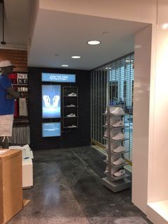 A store interior with shoe displays, a man in a blue shirt, and a shiny white wall.