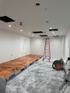 Room under construction with exposed wooden subfloor, recessed ceiling lights, ladder, and saw.