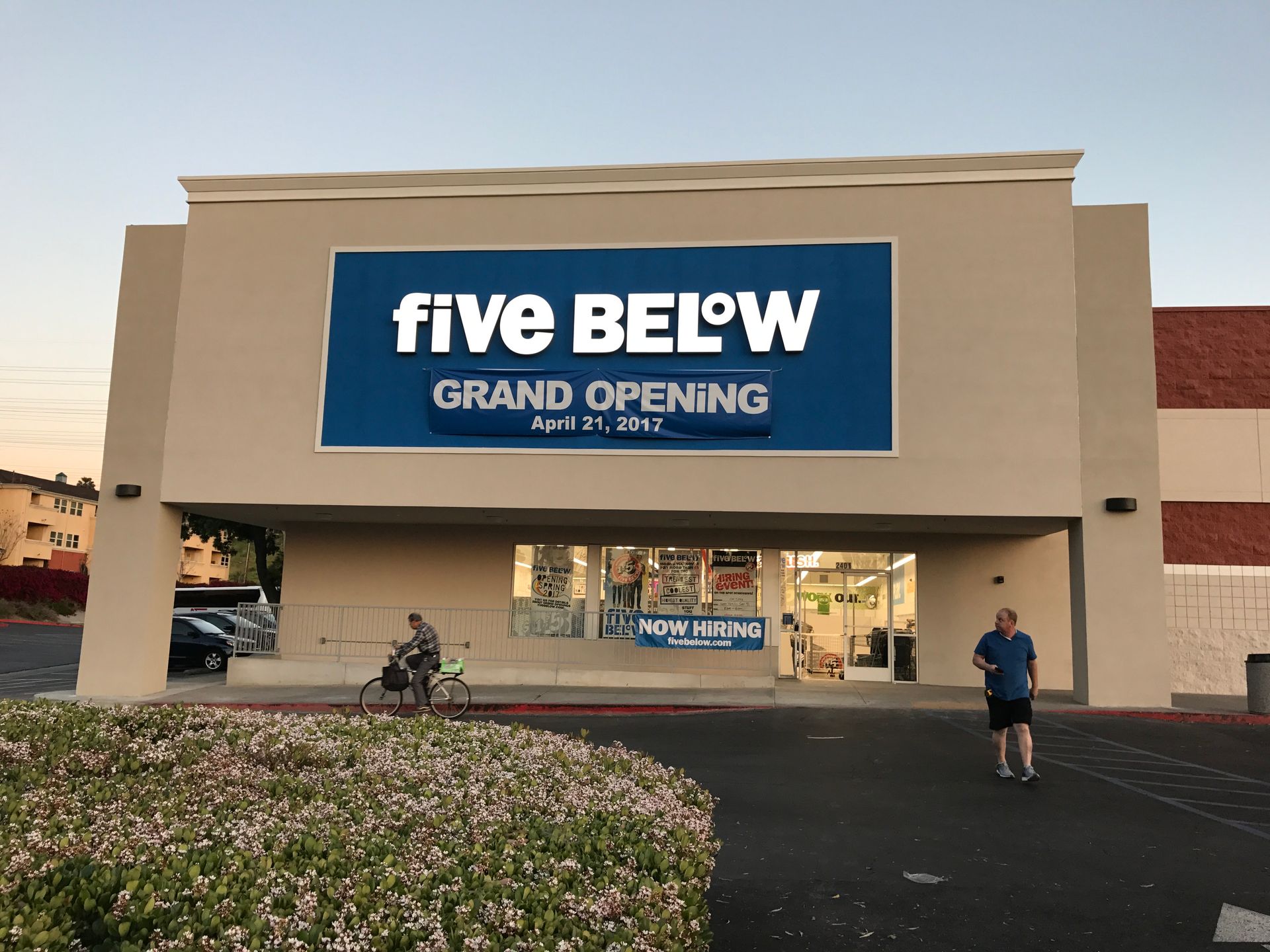 Five Below store exterior with grand opening sign; person biking, another walking.