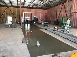 Interior view of a building under construction, with wet concrete floor and workers in the background.
