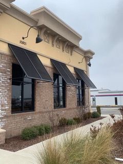 Building exterior with brick and tan walls, black awnings over windows, and a cloudy sky.