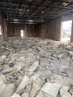 Interior demolition site with debris covering the floor, exposed walls, and ceiling beams.