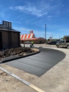 Freshly poured concrete driveway curves toward a building under construction, with a Whataburger in the background.
