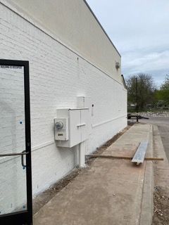 Exterior of a white-painted building with a door, electrical box, and a concrete ramp.