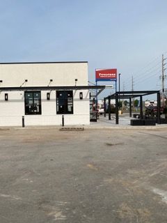 A modern building with black trim, pergola, and Firestone sign in the background.