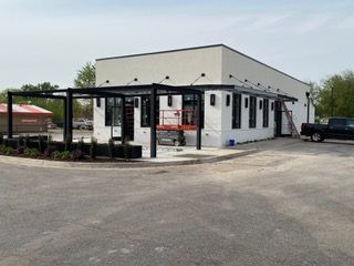 Modern white building with black accents, awning, and outdoor pergola. Construction equipment present.