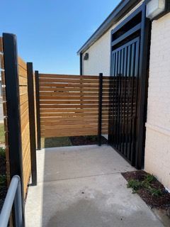 Wooden and black metal privacy fence next to a building entrance on a concrete path.