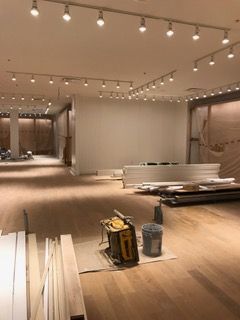 Interior construction: Empty room with overhead lighting, wood floors, and building materials.