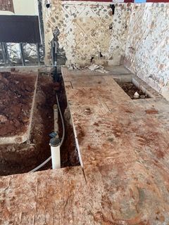 Construction site: open trench with pipes, exposed brick wall and a partially demolished floor.