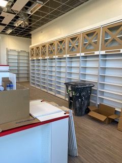Empty store interior with shelves and decorative wooden panels. Trash can and boxes on the floor.