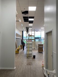 Interior view of a store under construction; a person on a ladder working on the ceiling.
