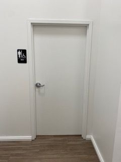 White door with accessible restroom sign. Silver handle. White walls, wooden floor.