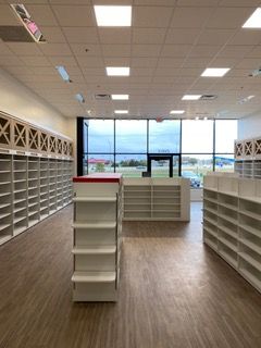 Empty retail space with shelving and large windows. Wooden floors, white walls and shelving.