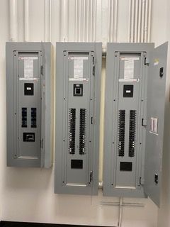 Three gray electrical panels mounted on a white wall, one door open.