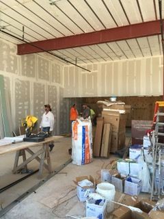 Interior of a building under construction. Workers are present. Drywall is being installed; materials scattered around.