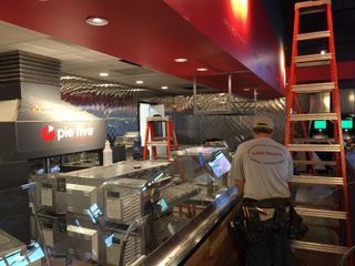 Restaurant kitchen under construction; worker on ladder, stainless steel surfaces, red ceiling.