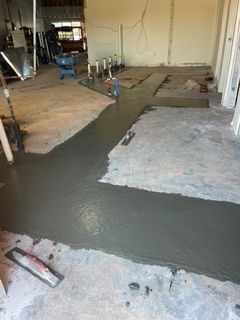 Concrete floor being poured; construction site interior. Gray cement with trowel present.