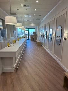 Long, narrow retail space with white counters and paneling, wood-look floor, mirrors.