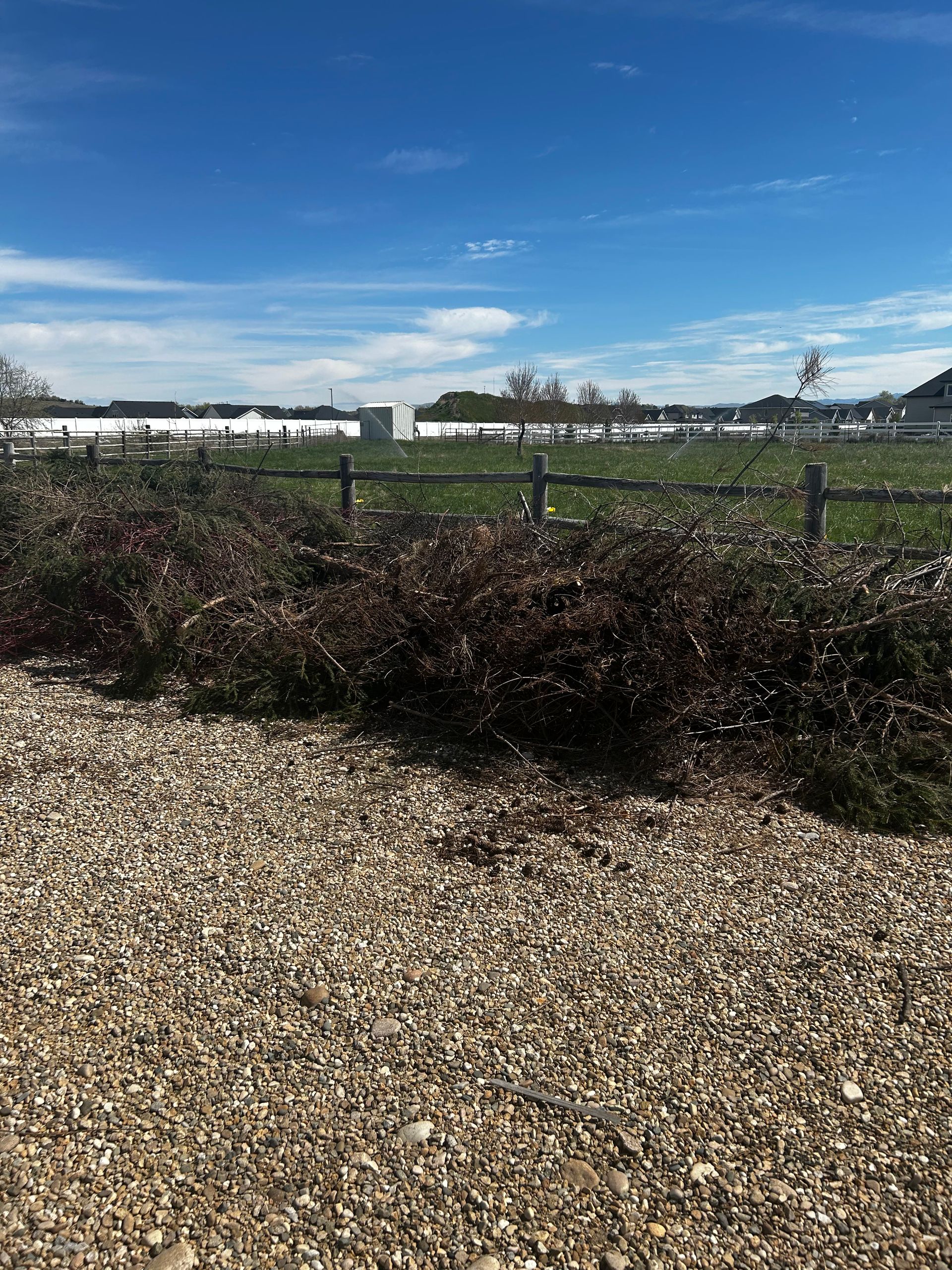 A gravel road with a fence in the background and a field in the background.