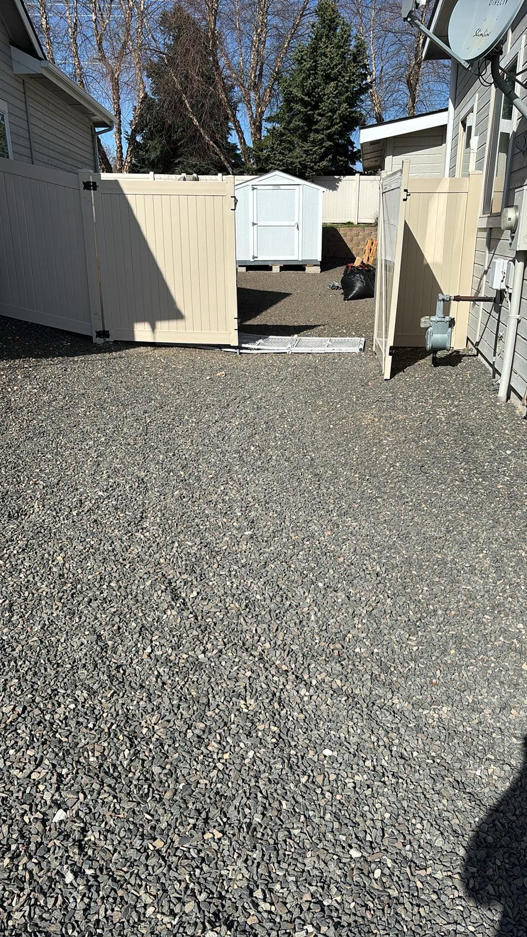 A gravel driveway leading to a house with a wooden fence.