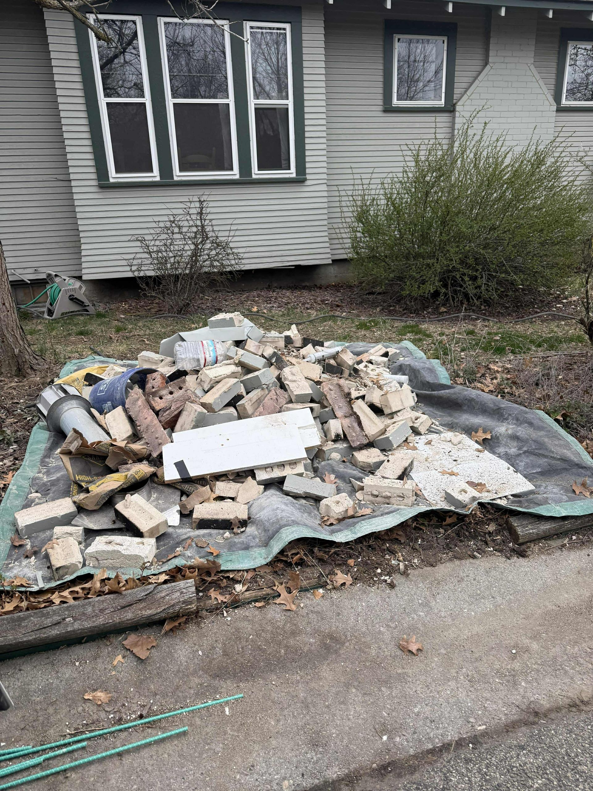 A pile of bricks is sitting on the side of the road in front of a house.