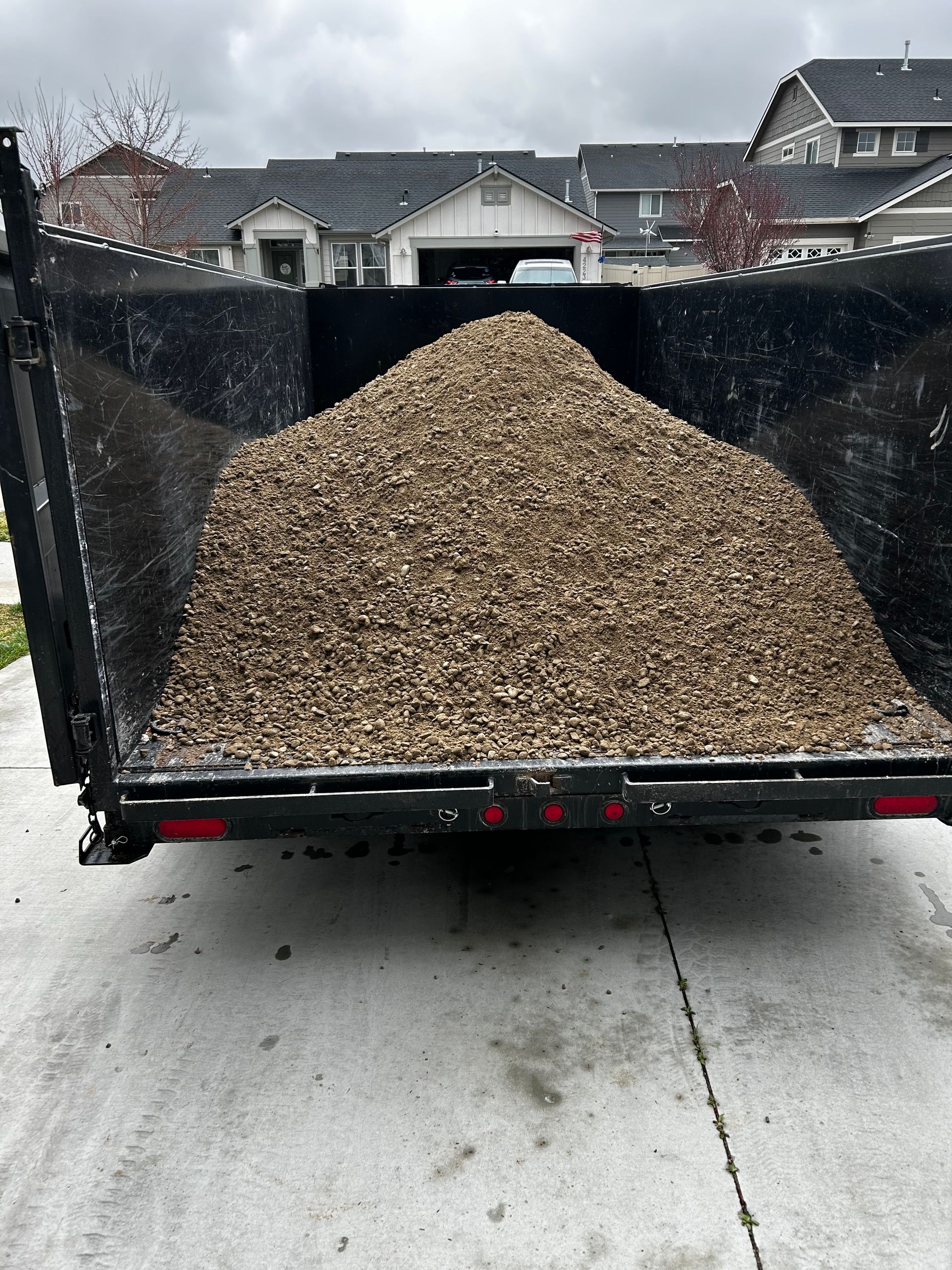 A dumpster filled with gravel is parked on the side of the road.