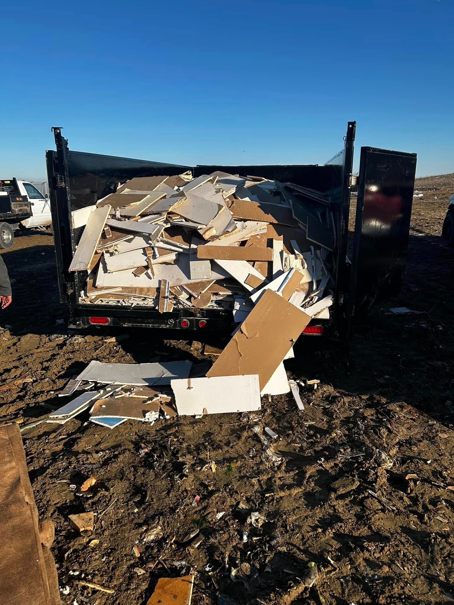 A dumpster filled with cardboard boxes is sitting in a dirt field.