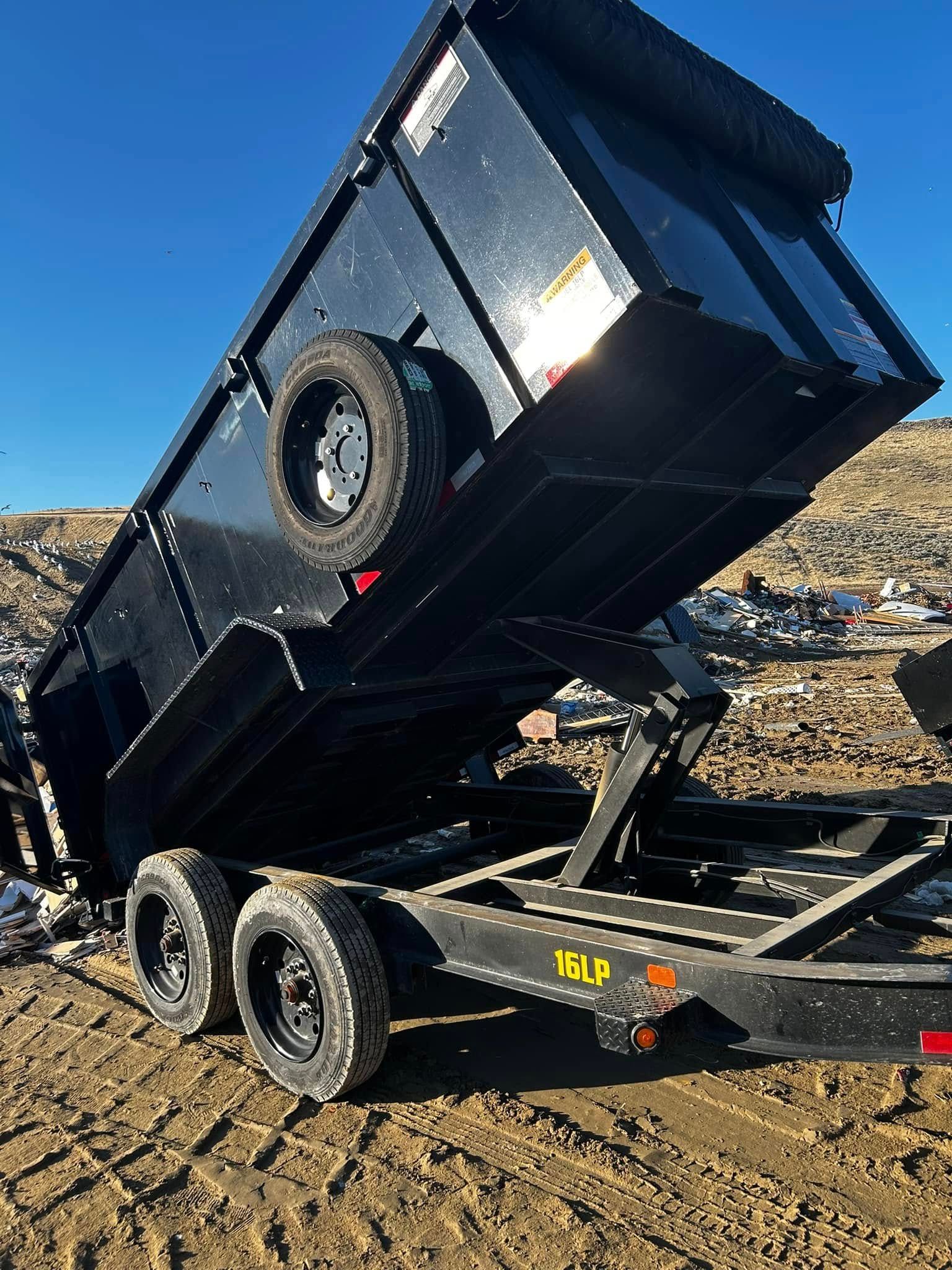 A dumpster is sitting on top of a trailer in a dirt field.