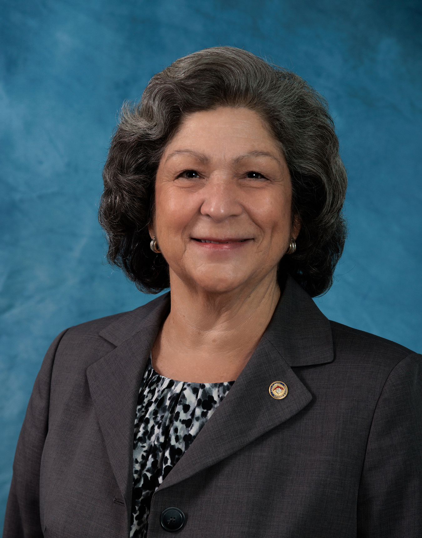 A woman wearing a gray jacket and a black and white dress smiles for the camera