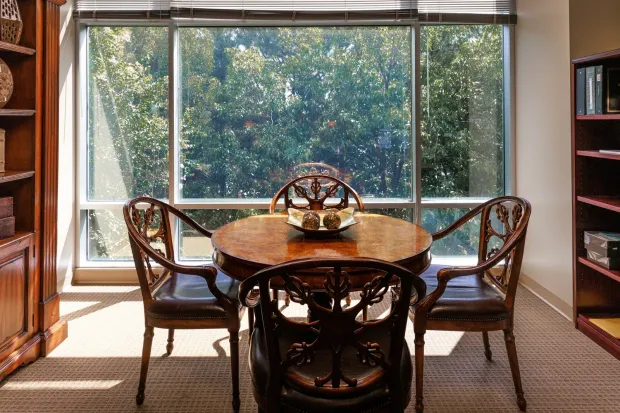 Cozy dining nook with round wooden table, two chairs, and large sunlit window overlooking trees