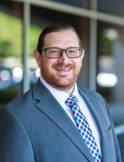 Smiling man in a blue suit and glasses standing outdoors