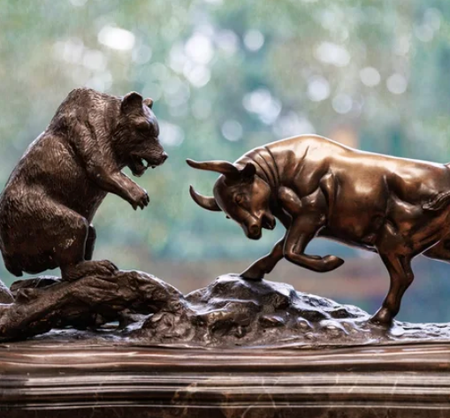 Bronze bear and bull statues facing off on a reflective surface with blurred background