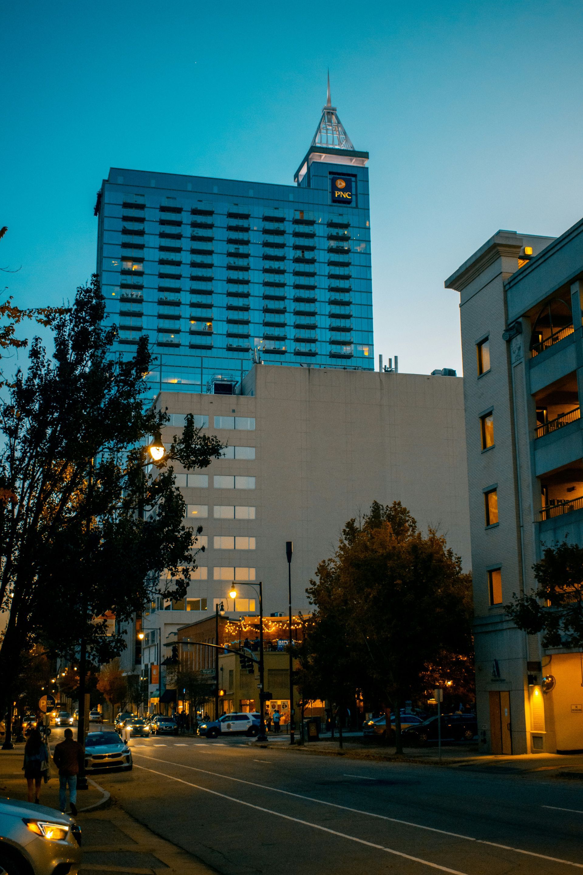 City street at dusk with tall modern buildings and lit windows under a blue sky