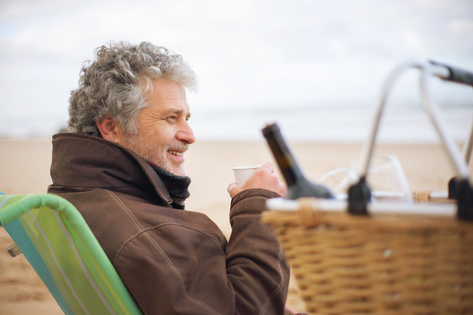 Man sitting in a chair on a boat, holding a cup and smiling in a wicker-lined outdoor setting