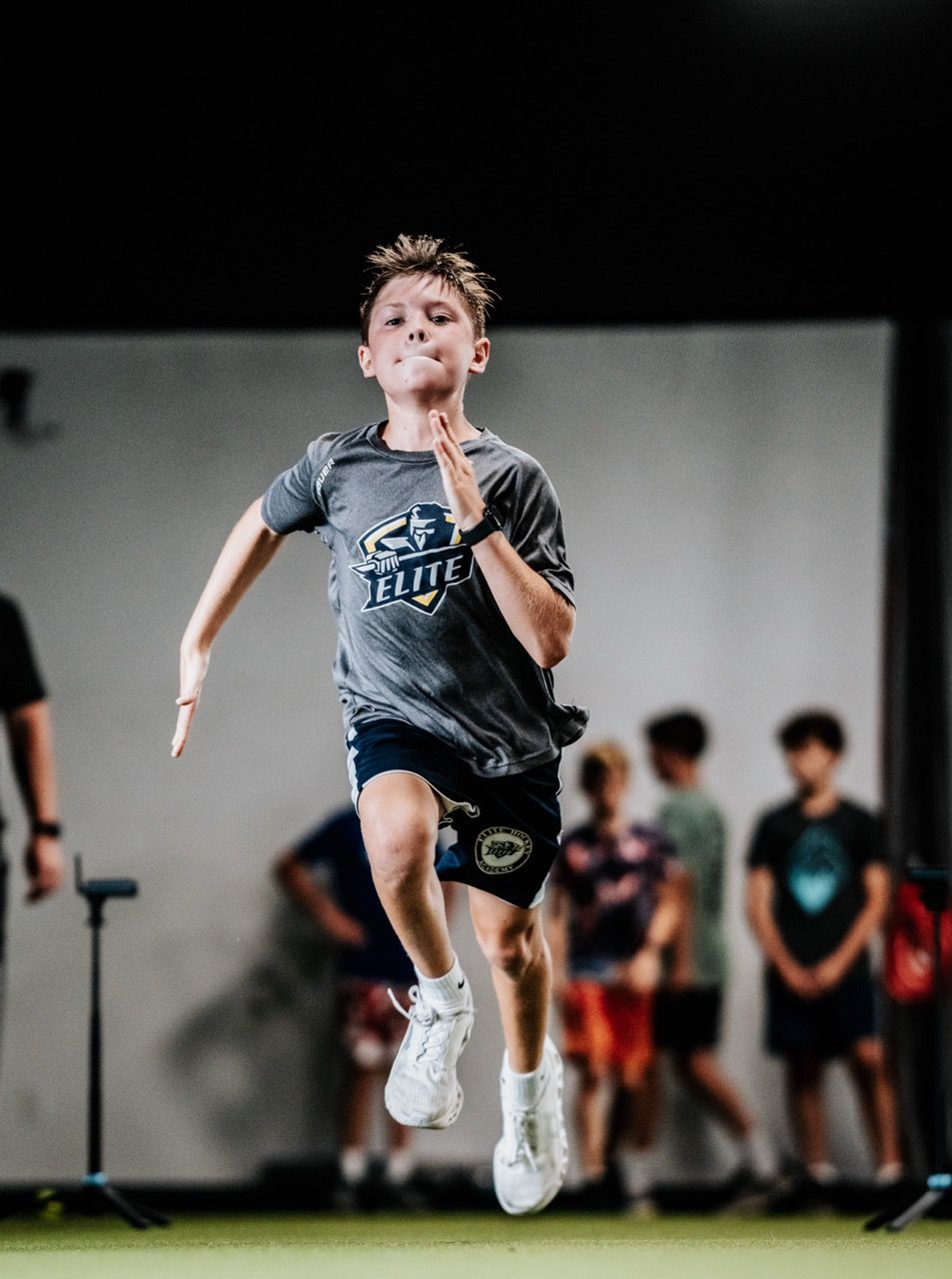 Young athlete sprinting indoors during a track event, with blurred competitors in the background