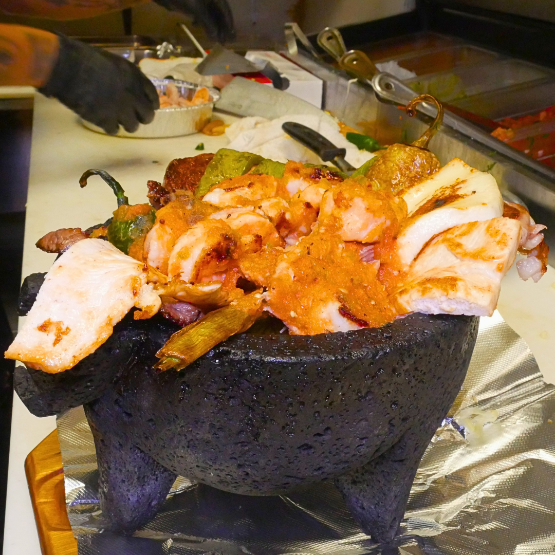 Molcajete - grilled chicken, ribeye steak, shrimp, chorizo, nopales in volcanic stone bowl with Oaxaca cheese, jalapeños, rice, beans, guacamole, tortillas.