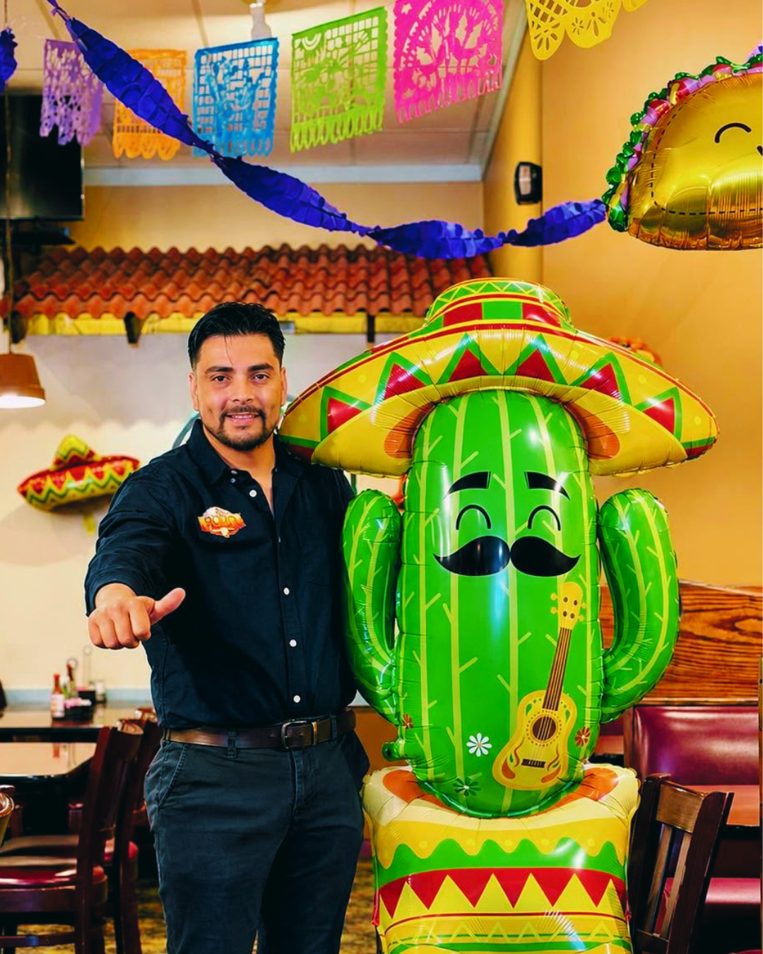 Man standing beside a colorful cactus decoration in a festive restaurant