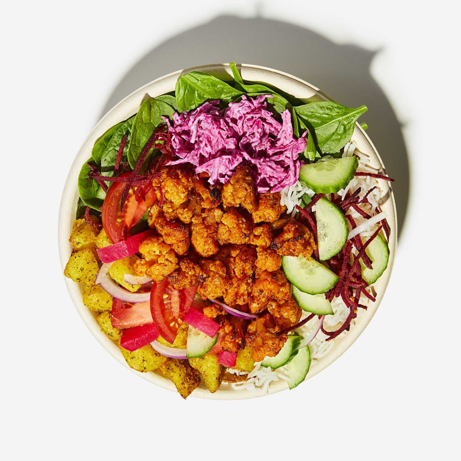 A bowl of food with vegetables and meat on a white surface.