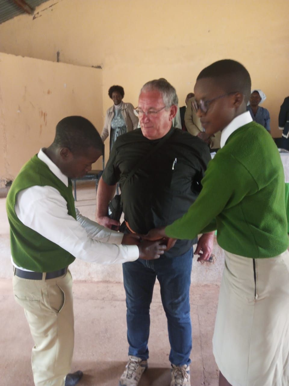 A man in a black shirt is being helped by two men in green vests
