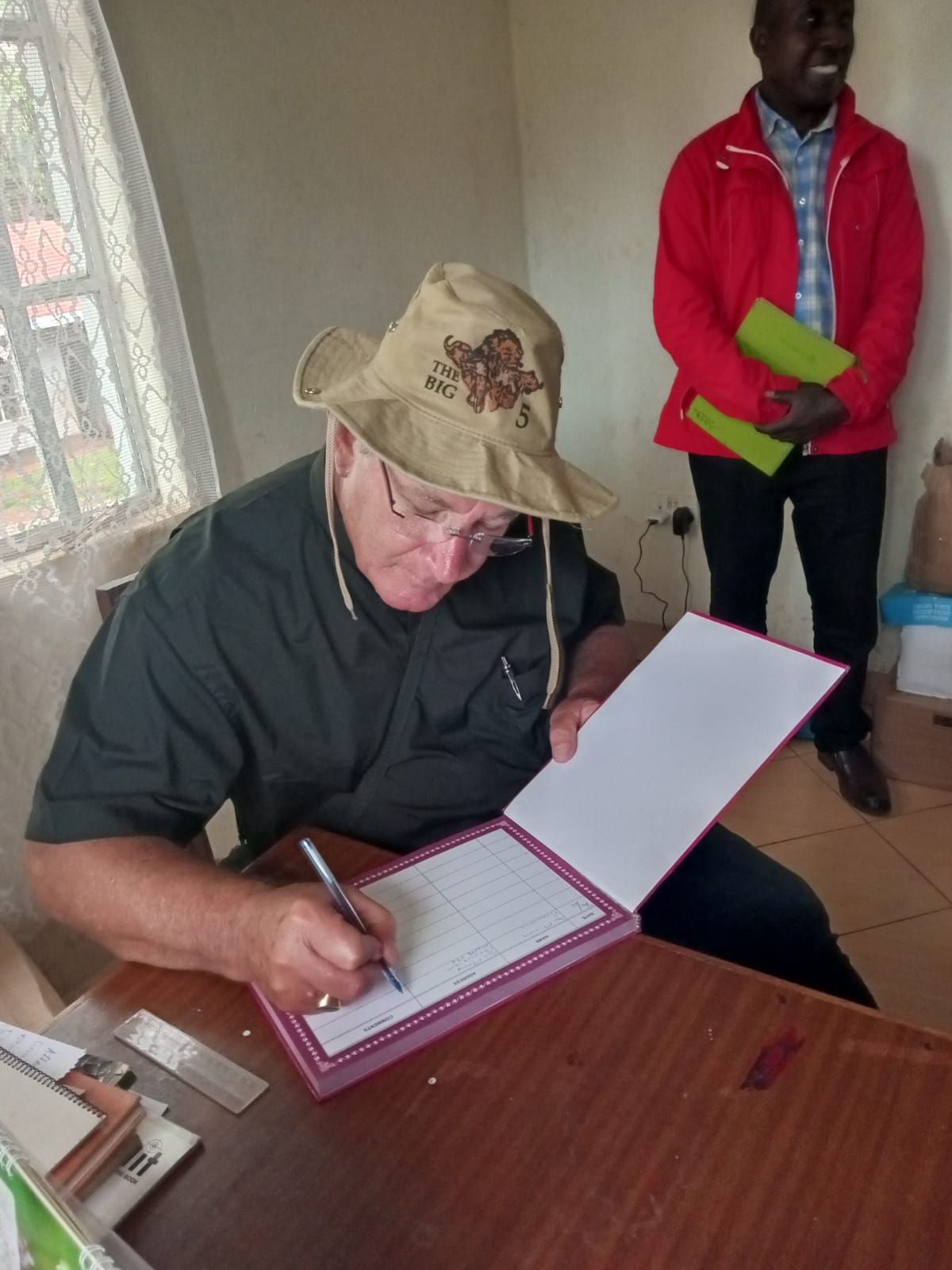 A man wearing a hat is writing on a piece of paper.