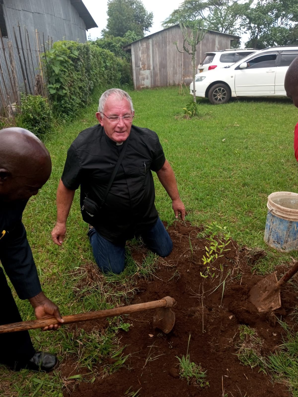 A man is kneeling down in the dirt holding a shovel.