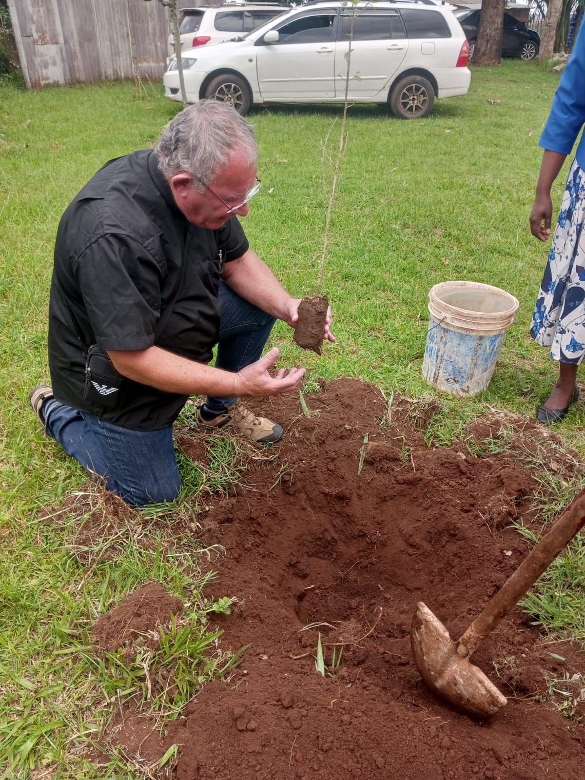 A man is kneeling down in the dirt to plant a tree.