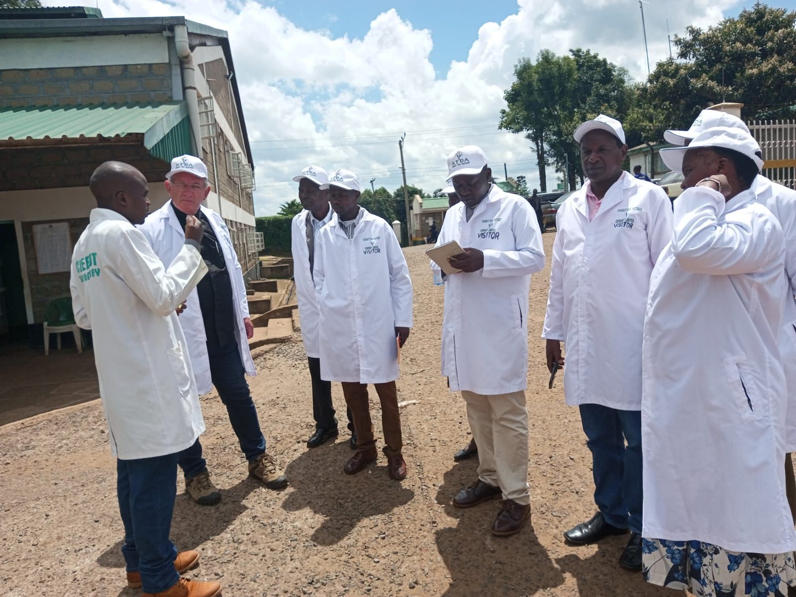 A group of people in white coats are standing in a dirt field.